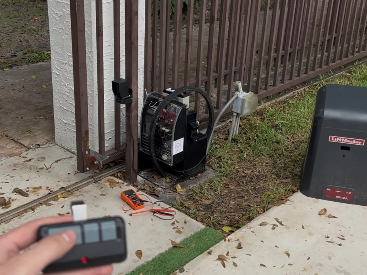 Testing a newly fitted gate operator on the handheld remote at handover, with the brown iron gate behind