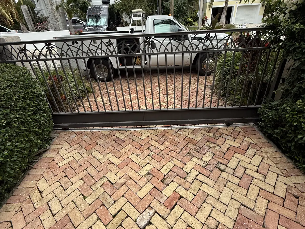 Ornamental iron driveway gate closed across a herringbone brick paver entrance, with a CMC truck parked beyond it