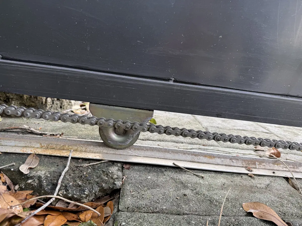 A slack drive chain hanging below a sliding gate beside the V groove wheel and the ground track