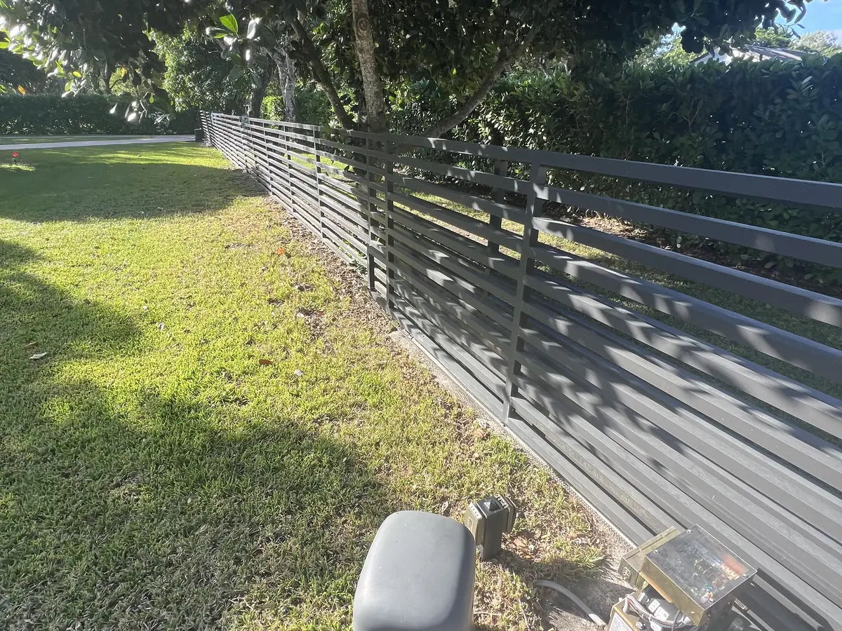 Horizontal slat aluminum gate running along a lawn edge, with the slide operator on its concrete pad and the control box open beside it