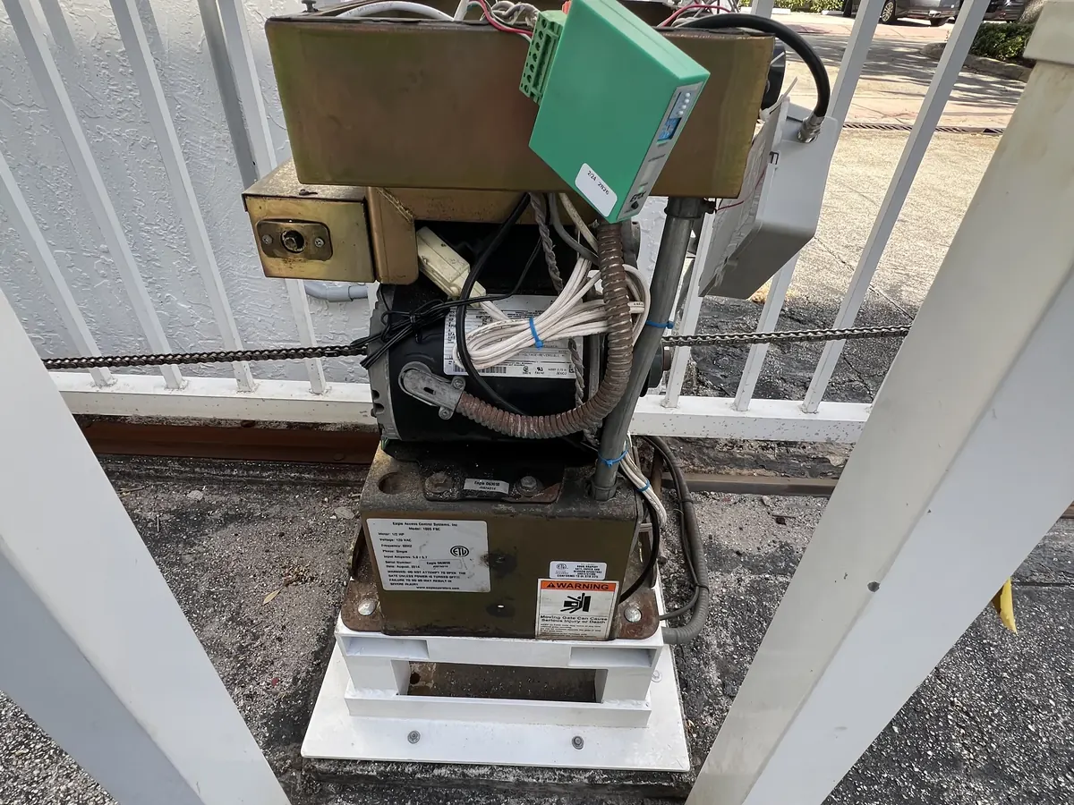 Slide gate operator and its control box mounted behind a white picket gate at an apartment entrance