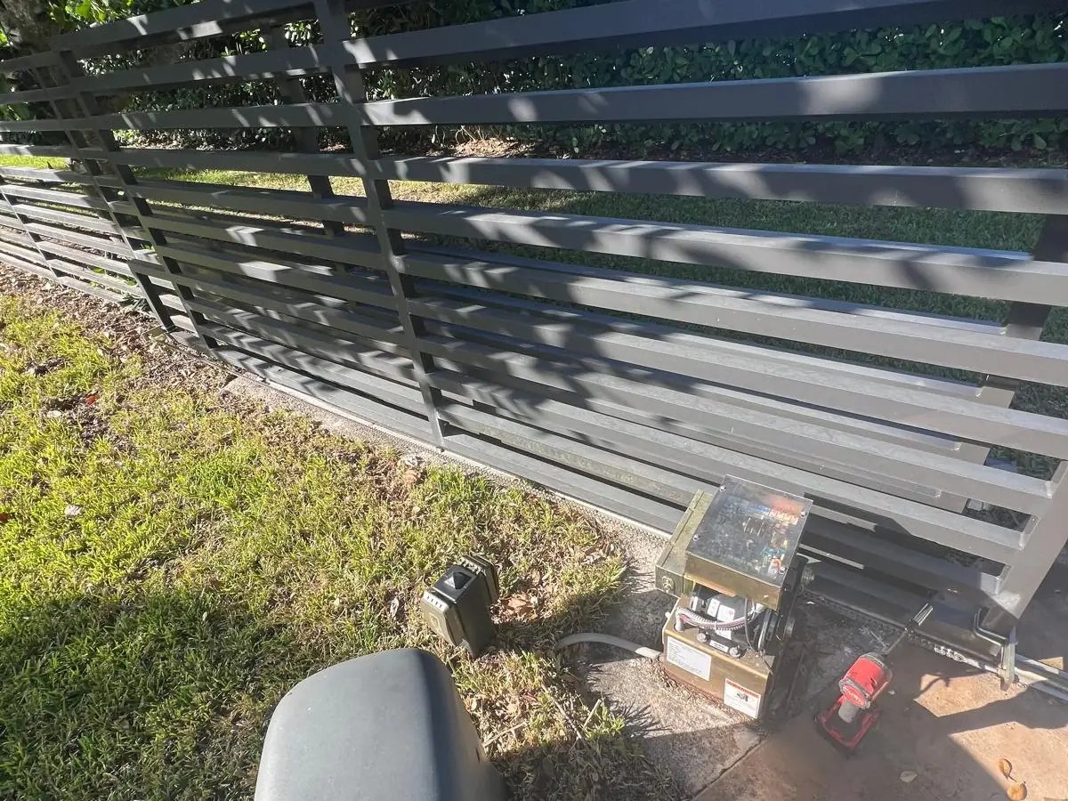 Slide gate operator installed on its pad at the end of a horizontal slat aluminum gate