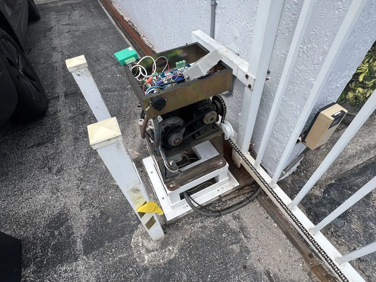 Slide gate operator with its cover off, the drive gear meeting the rack along the bottom rail of a white gate