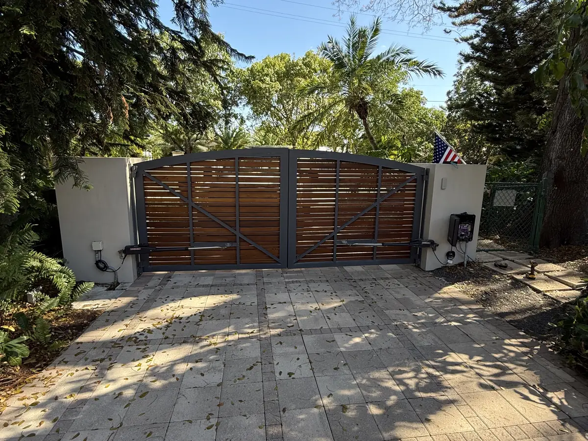 Horizontal wood slat swing gate hung between white stucco pillars, closed across a tiled driveway
