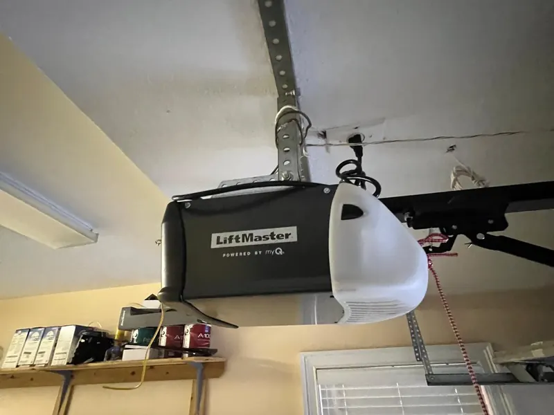 A LiftMaster garage door opener mounted to a garage ceiling with its hanging bracket, rail and light lens visible