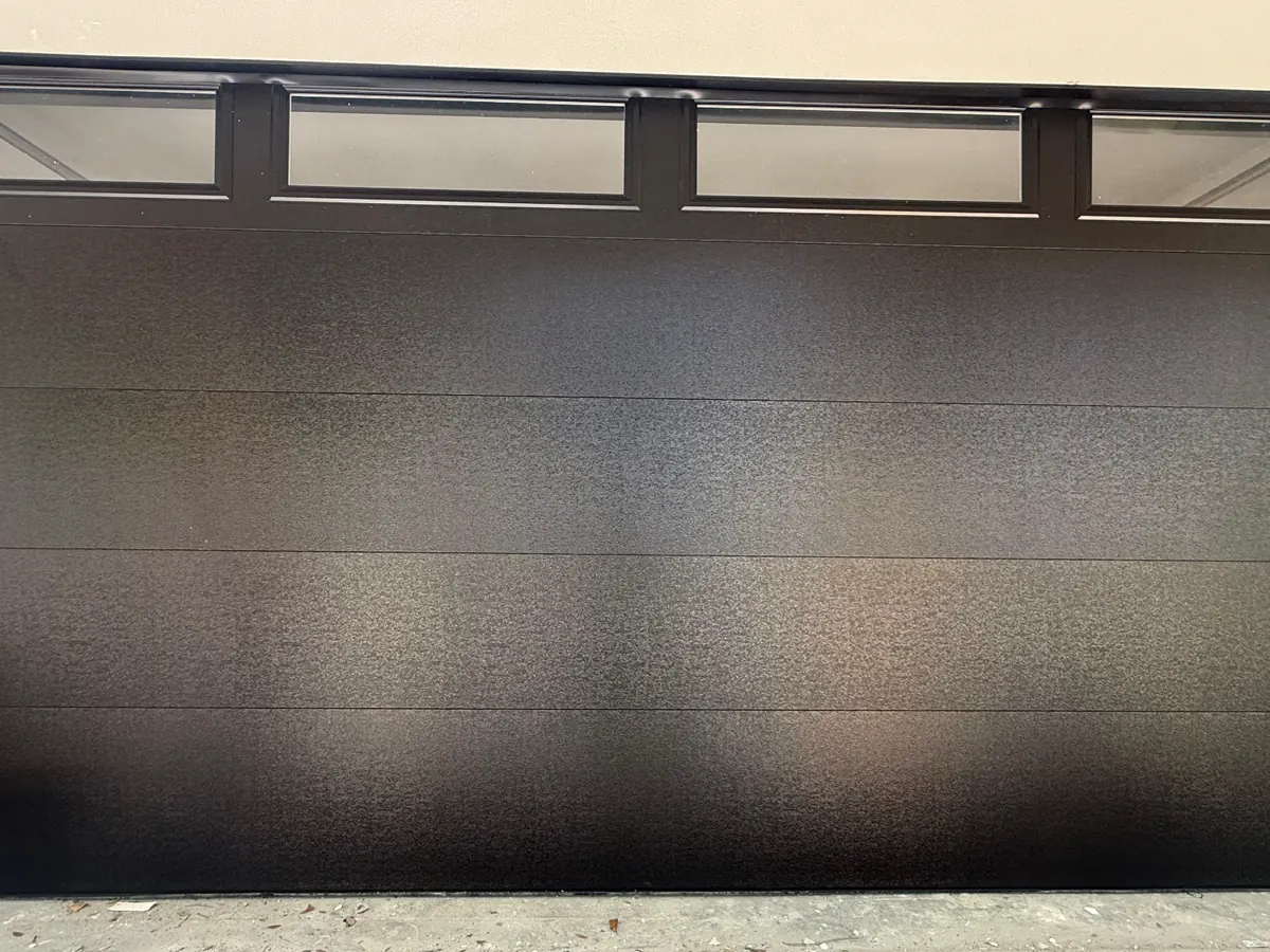 Black flush panel double car garage door with a row of frosted windows across the top section