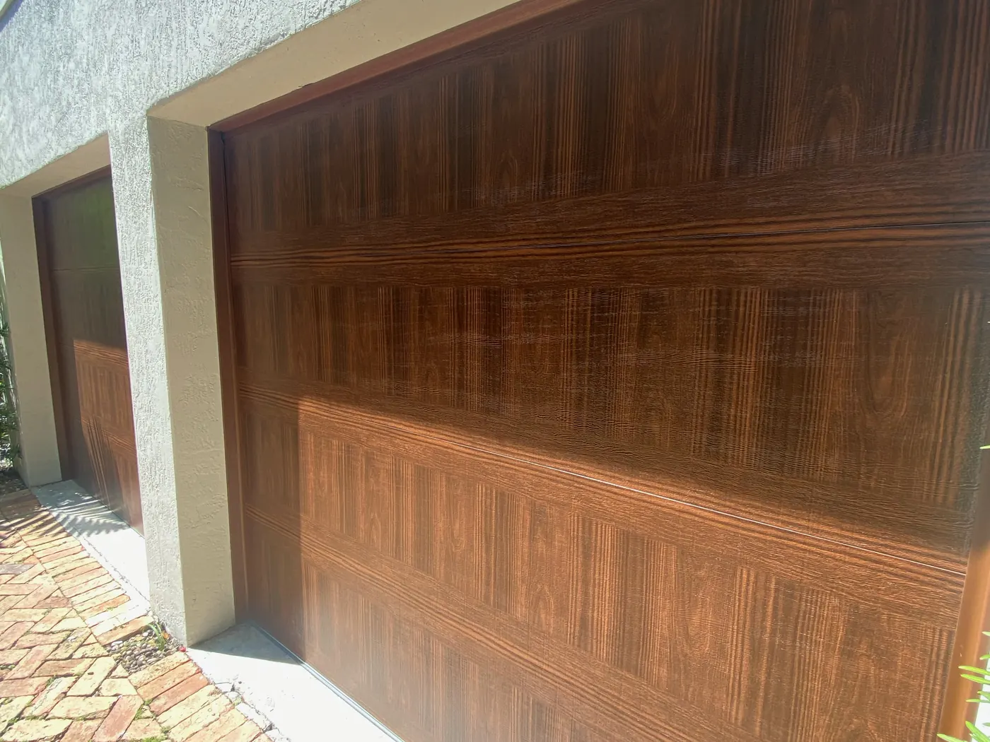 A flush panel garage door in a walnut woodgrain finish above a brick paver driveway
