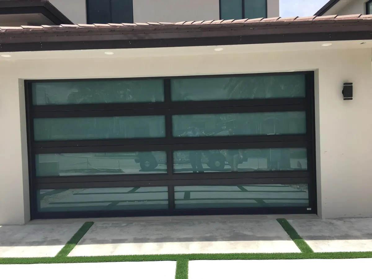 Full view glass garage door in a black aluminum frame on a contemporary home with planted driveway strips
