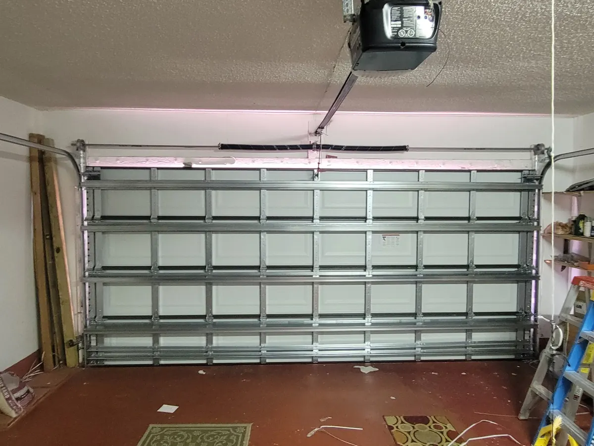 White short panel garage door seen from inside the garage, with the opener rail and workshop shelving