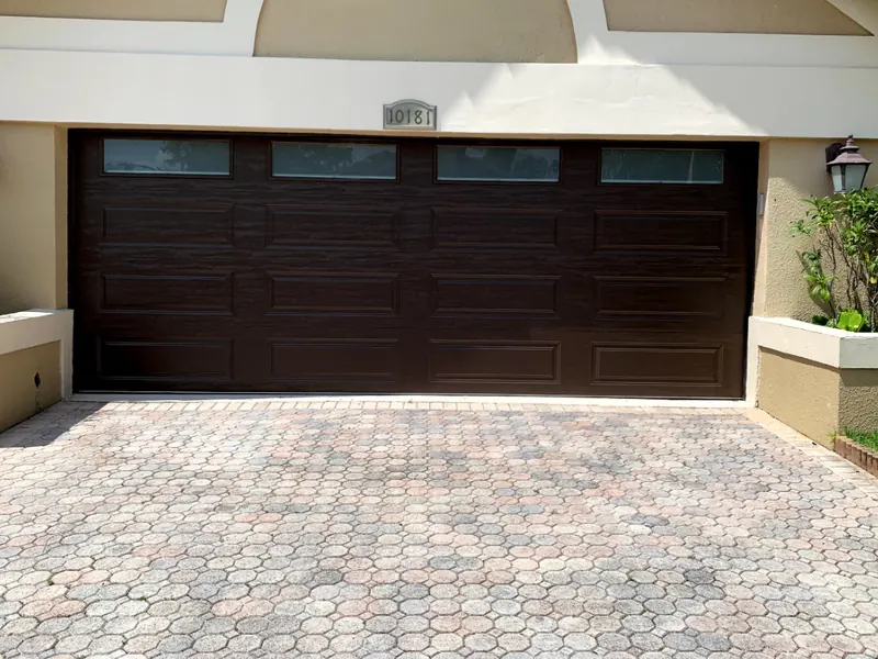 Dark brown long panel double garage door under an arched stucco trim