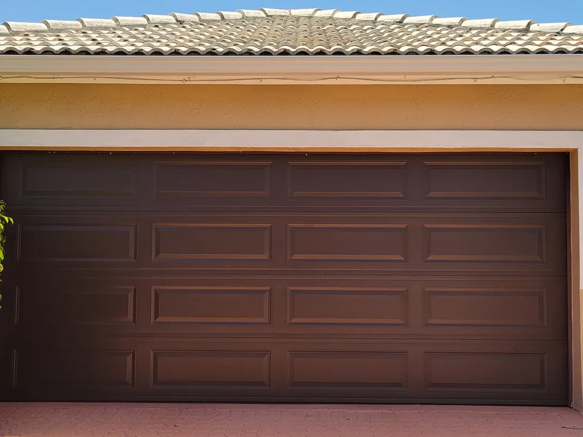 Brown long panel double car garage door on a stucco home, with hedging along the driveway edge