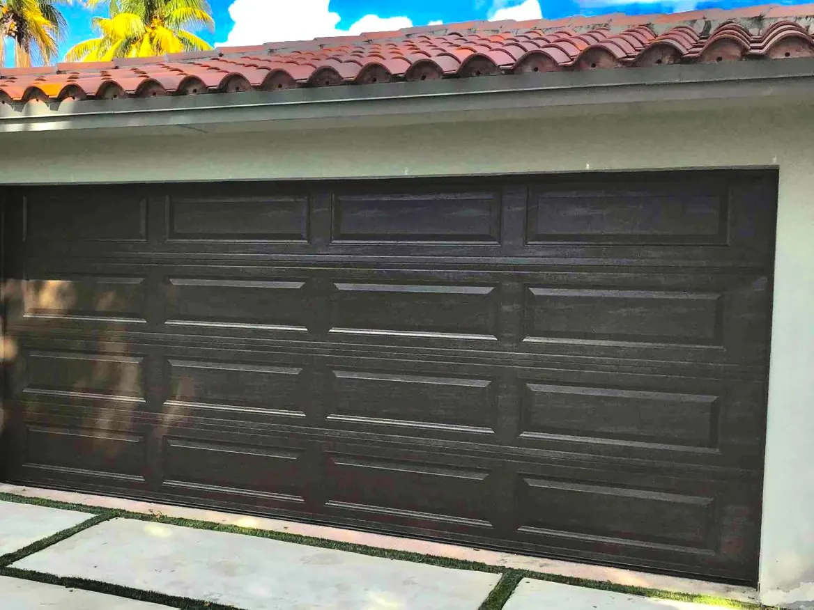 A dark brown long panel garage door on a white stucco home with a barrel tile roof