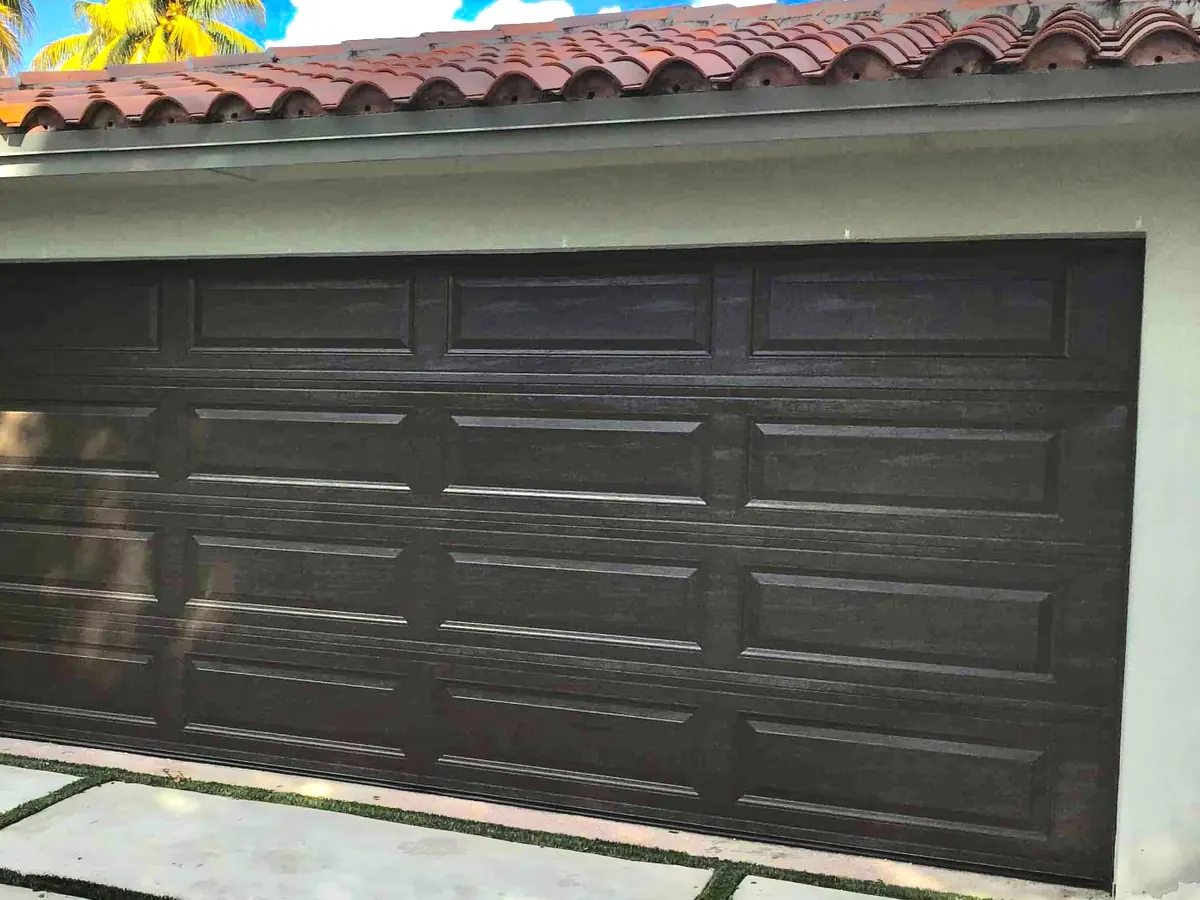 Dark brown long panel double car garage door on a stucco home with a barrel tile roof and palms overhead