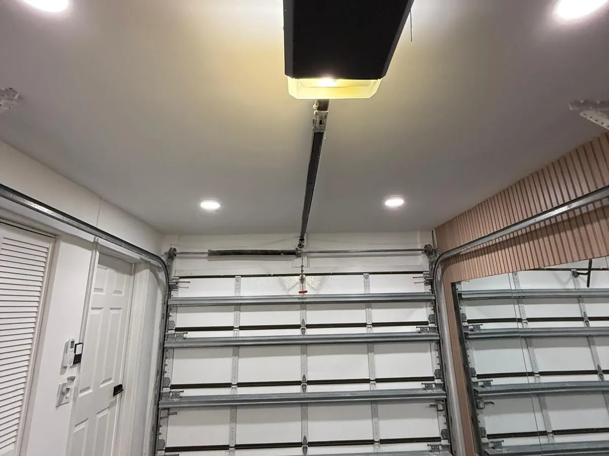 A newly installed ceiling mounted garage door opener with its rail running down to a white sectional door in a double bay garage