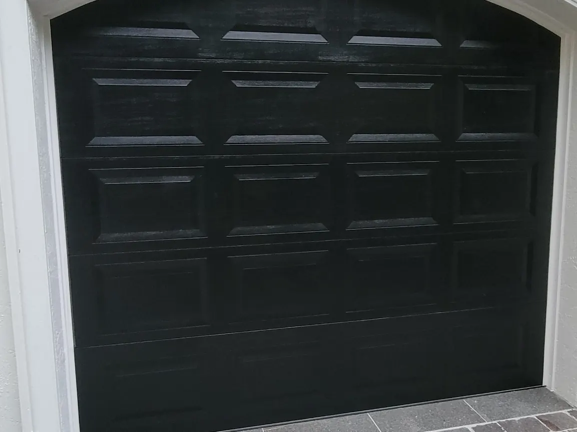 Black raised panel double car garage door set into an arched opening above a cobblestone driveway