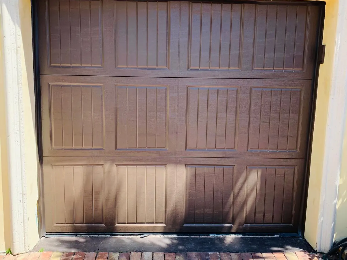 Brown raised panel single car garage door in a yellow stucco surround above a brick paver driveway