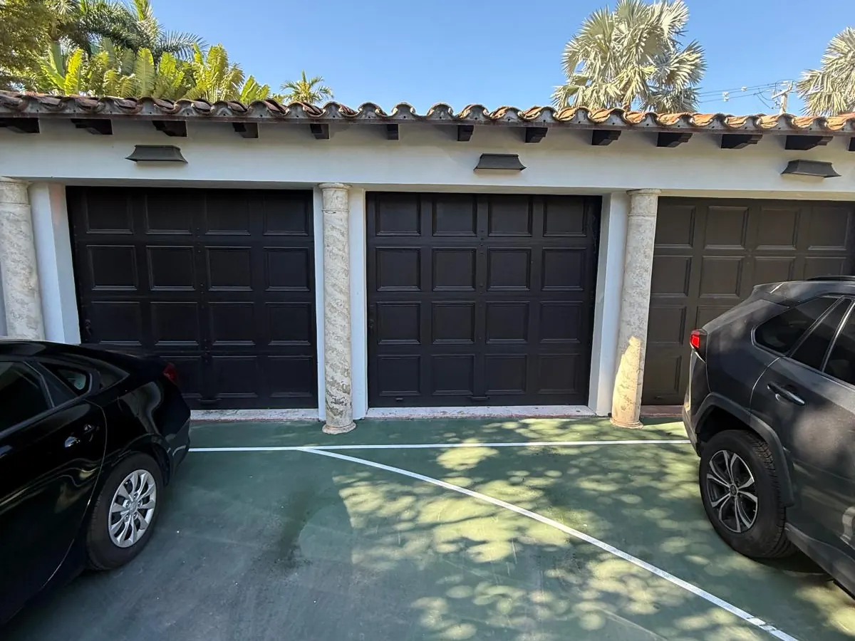 Three dark brown single car garage doors in a row under a barrel tile roof