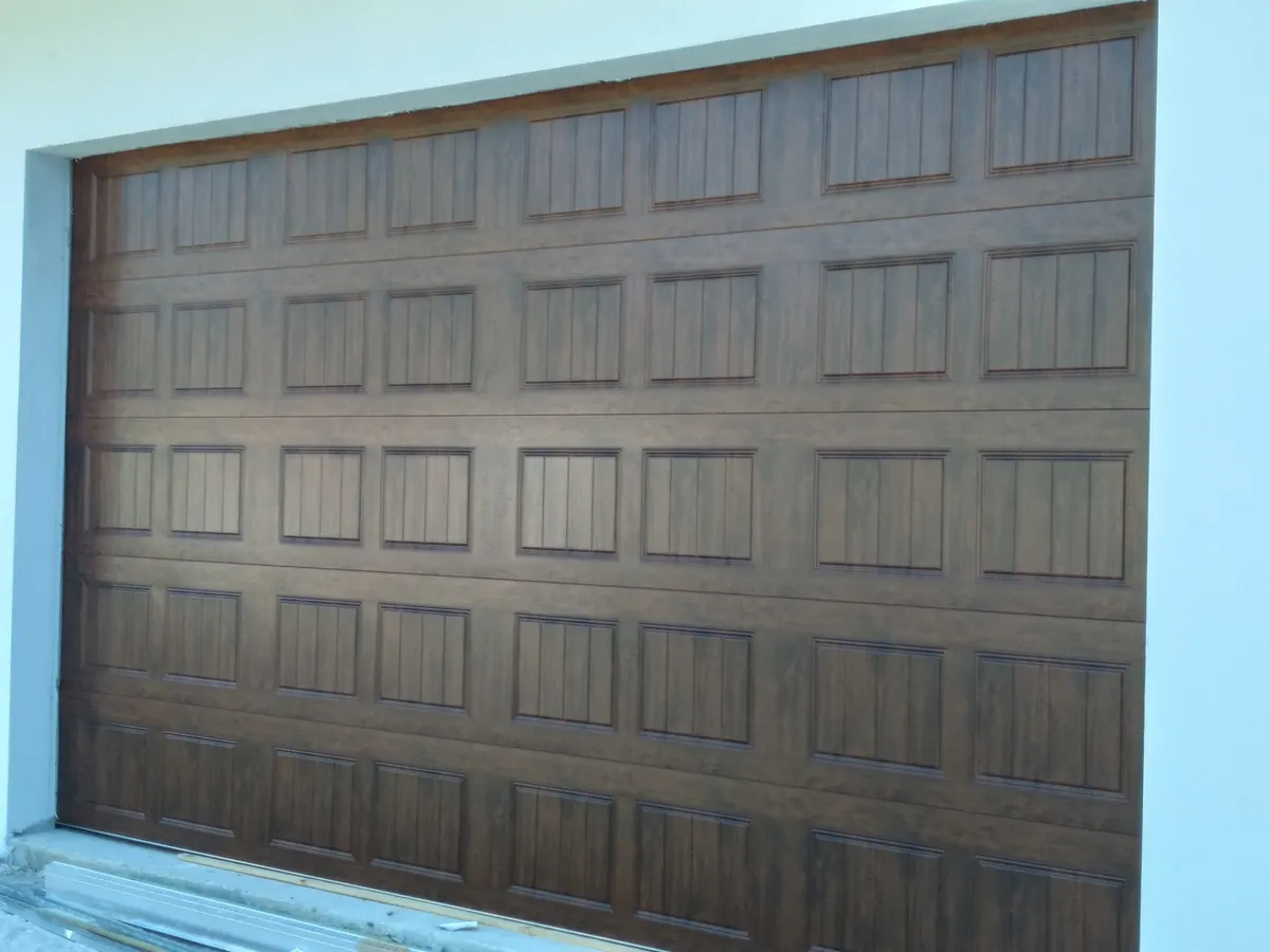 Walnut woodgrain raised panel double car garage door set into a turquoise painted wall
