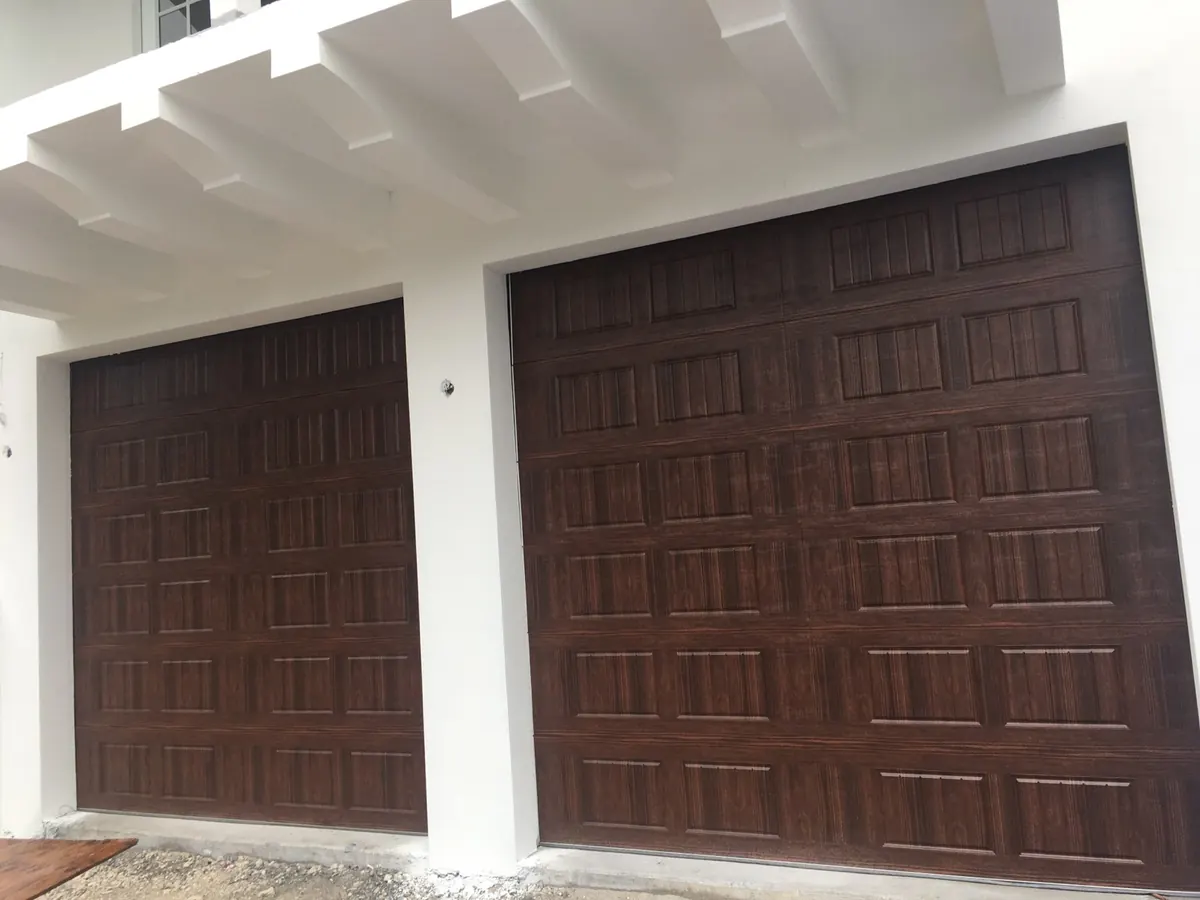 Two walnut woodgrain raised panel garage doors below a white pergola beam