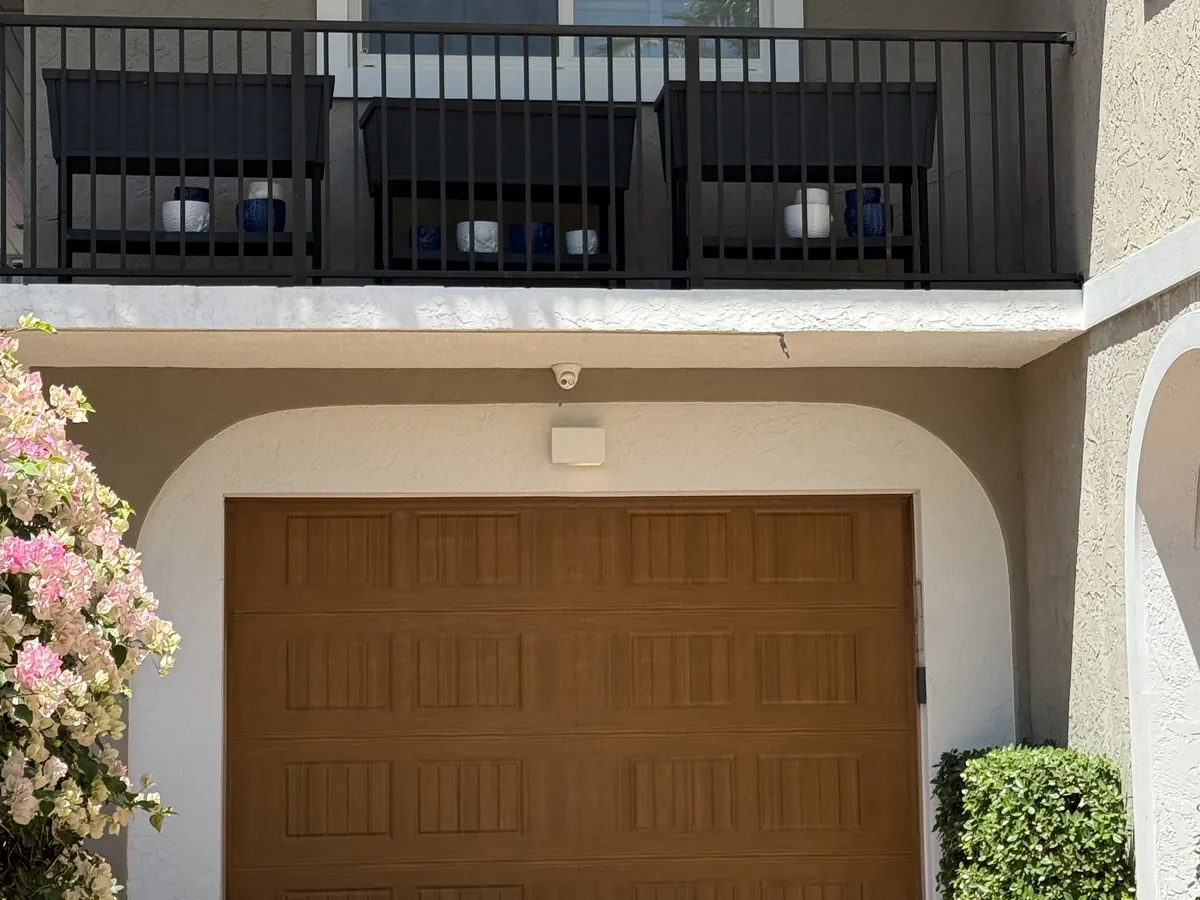 A single car woodgrain raised panel garage door under a balcony on a townhouse