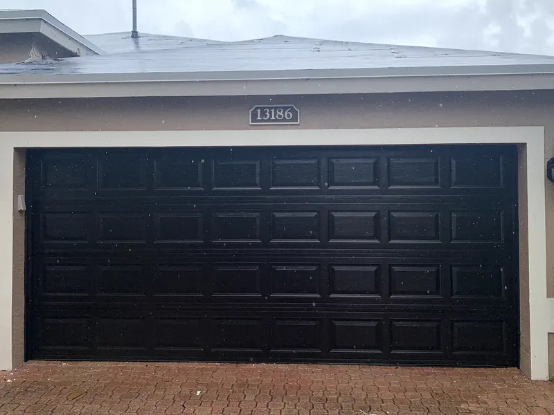 Puerta de garaje doble negra de panel corto sobre una entrada de adoquines, recién instalada