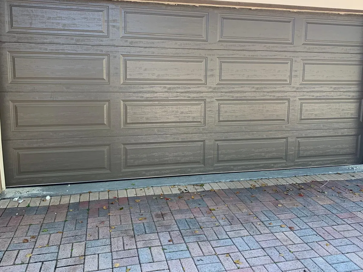 Taupe short panel double car garage door above a brick paver driveway