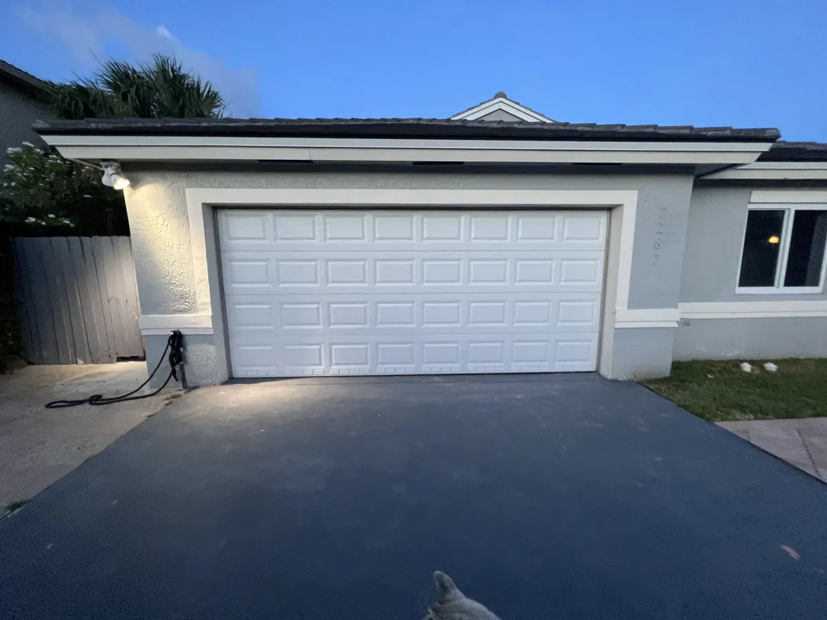 White double car garage door lit at dusk on a rendered home with a dark driveway