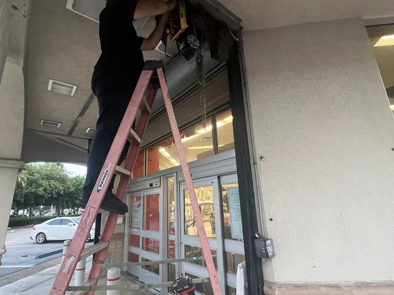 Technician on a ladder installing a rolling shutter on a storefront
