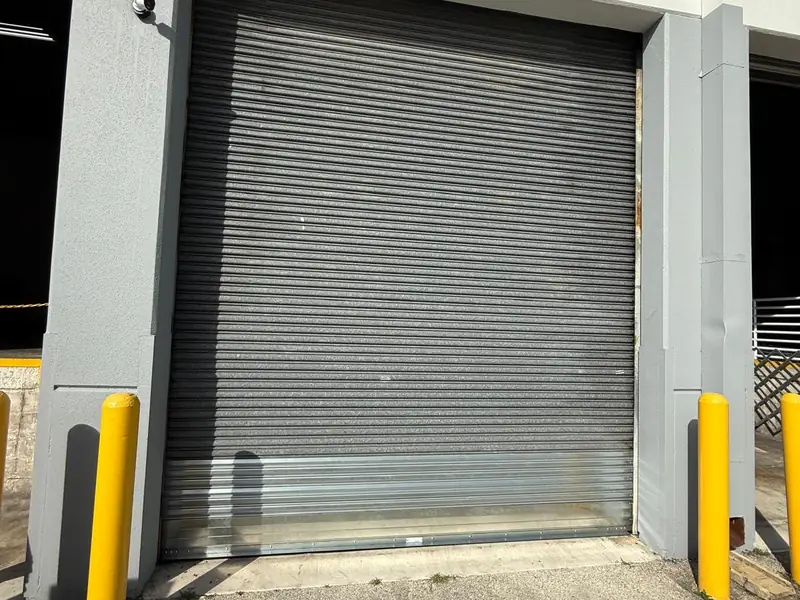 Grey commercial rolling steel service door closed in a loading bay opening between two yellow bollards