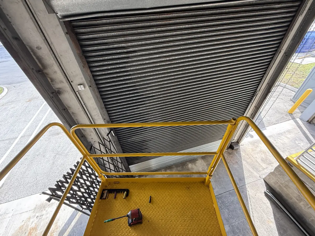 The underside of a rolling steel door curtain photographed from a raised work platform
