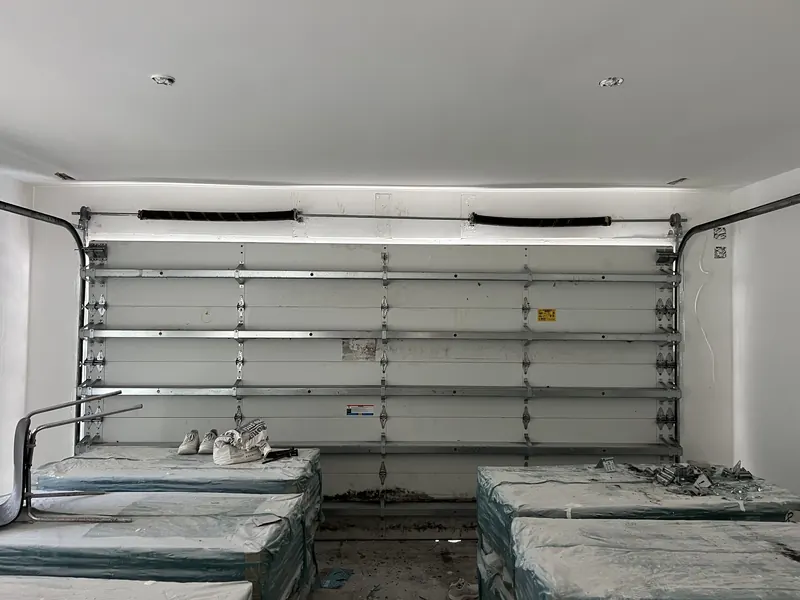 Interior view of a closed white sectional garage door showing its torsion springs, shaft and horizontal reinforcing struts