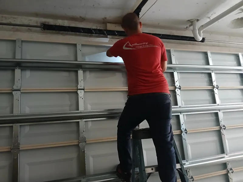 Técnico de CMC en una escalera colocando un refuerzo a una puerta de garaje desde adentro