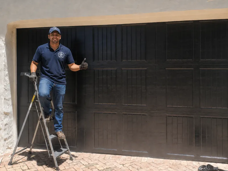 CMC technician with a ladder in front of a brown raised panel garage door after a service call