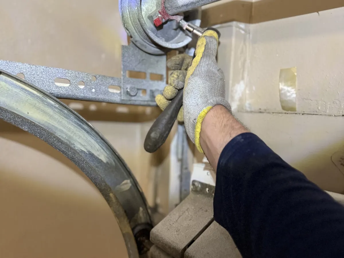 A technician turning a winding bar in the cone of a garage door torsion spring