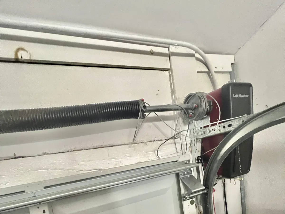 A LiftMaster wall-mounted opener installed beside the torsion spring and cable drum of a garage door