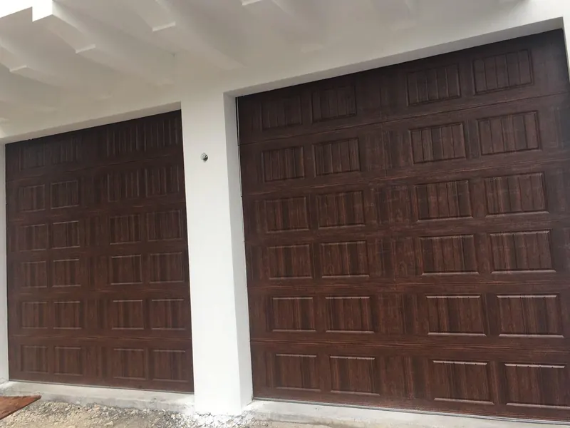 Two dark wood-grain steel garage doors on a newly built white stucco house, seen from an angle