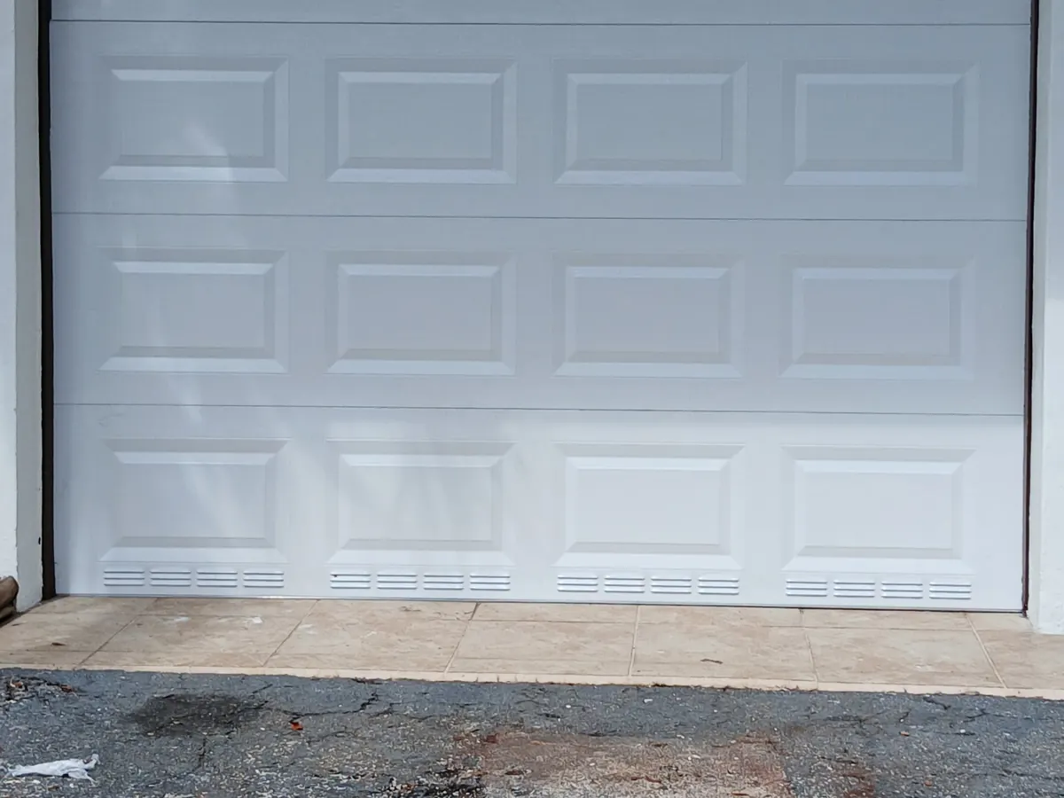 White raised-panel garage door with ventilation louvers across the bottom section, seen from the driveway