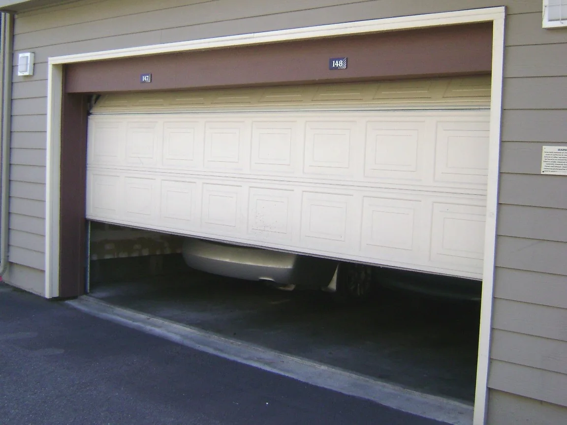 A white raised-panel garage door part way open, showing how the sections bend onto the horizontal track