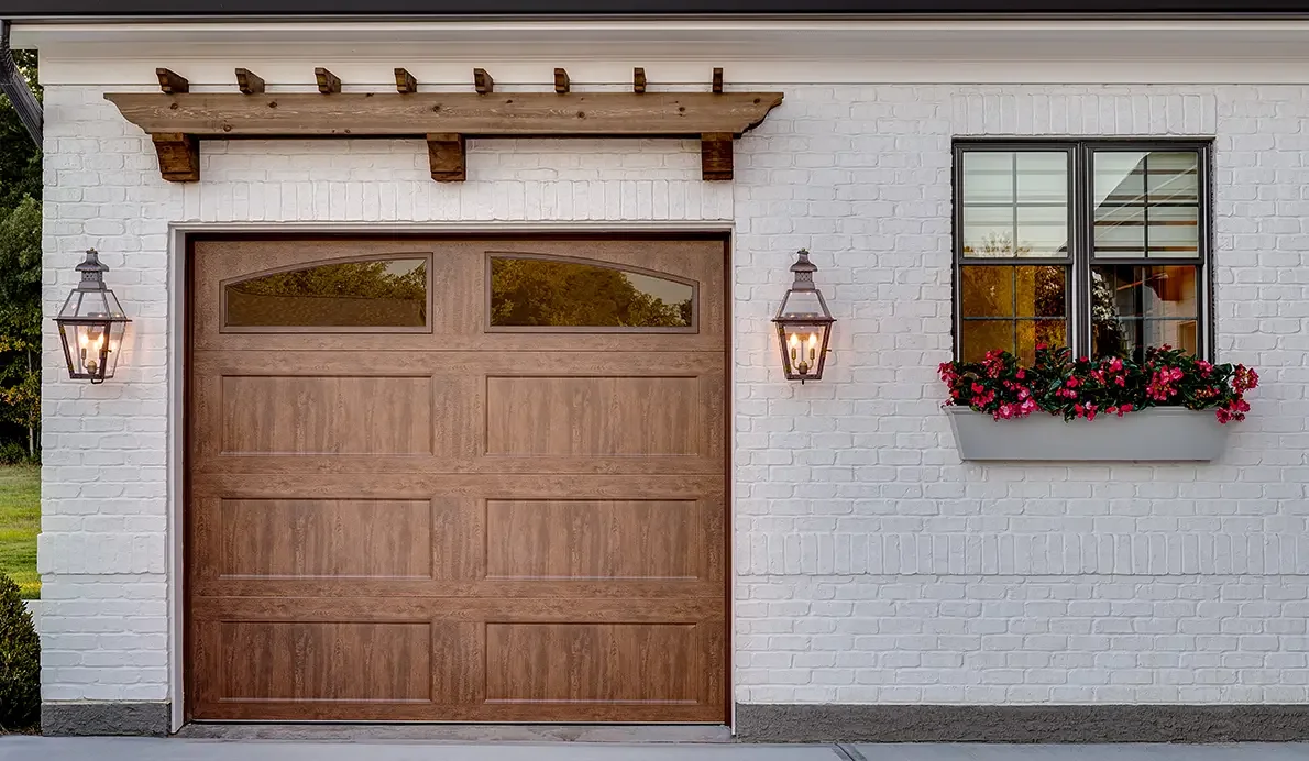 A wood carriage garage door on a white house with window boxes