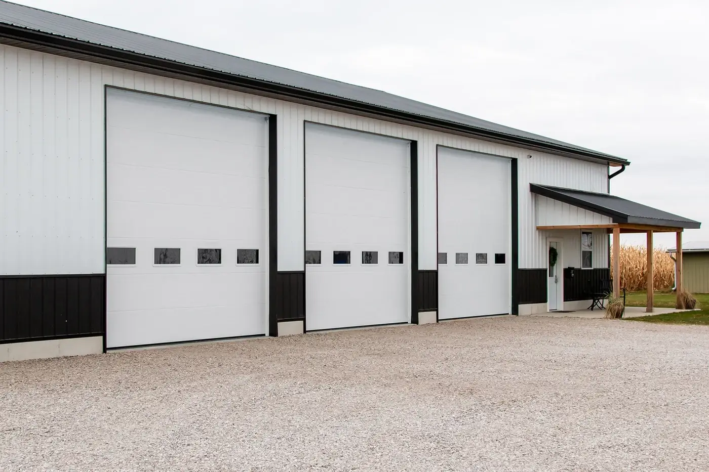 Three white commercial sectional doors with vision lights along a gravel service drive