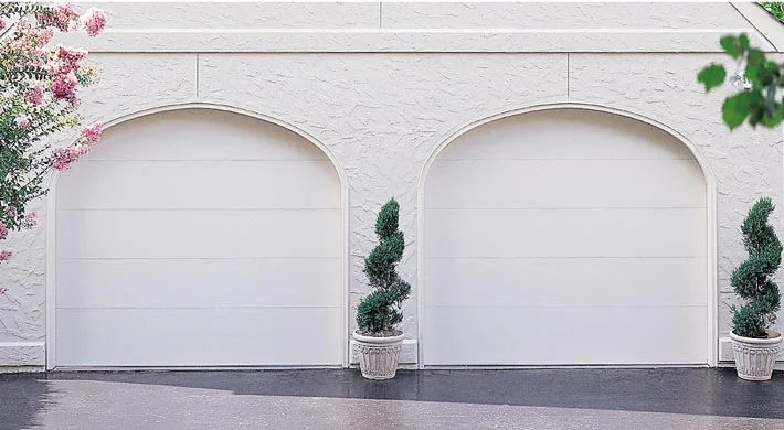 A pair of arched white garage doors on a stucco home