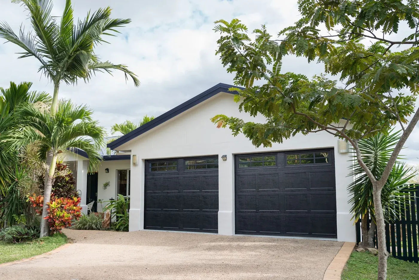 Two black garage doors on a pale stucco home framed by palms
