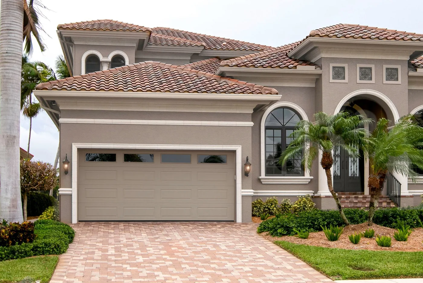 A Mediterranean style home with a tan garage door and paver drive