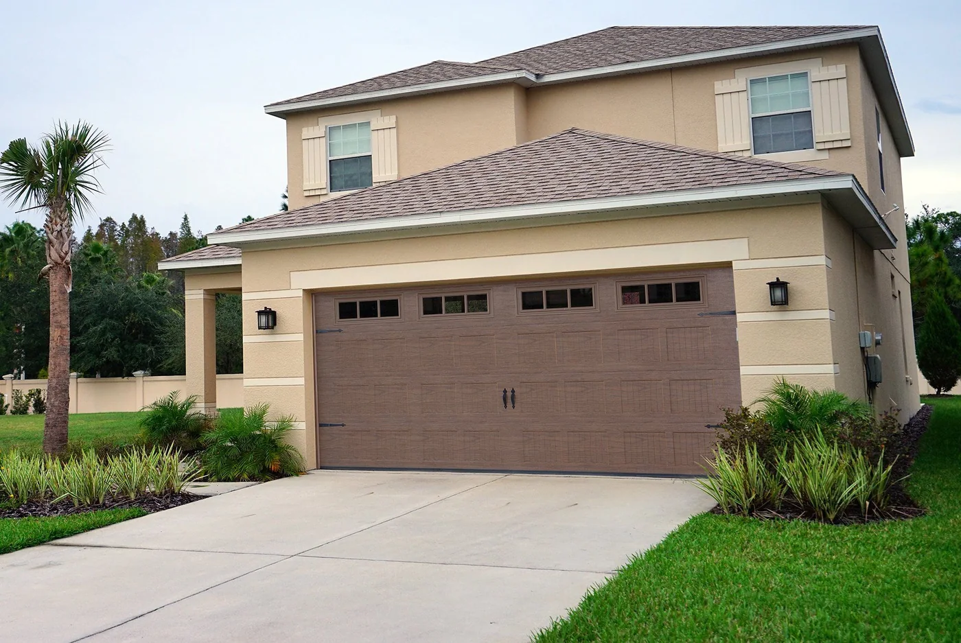 Tan stucco South Florida home with a brown double garage door and palms