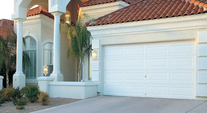 A tan stucco home with a barrel tile roof and a white double garage door