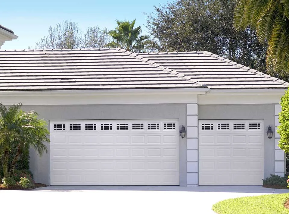 A barrel tile roof home with white garage doors and a curved drive