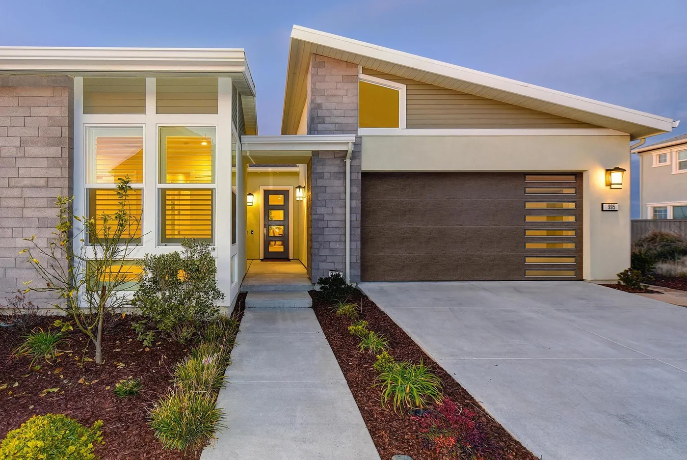 A contemporary home lit from within with a flush wood garage door