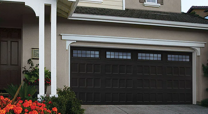 A modern grey house with a warm lit full view glass garage door