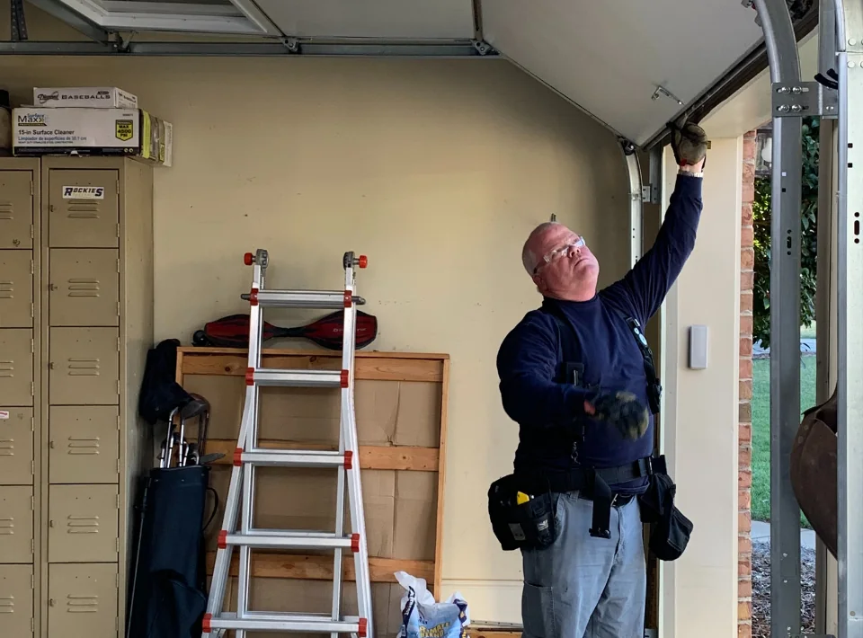 A technician on a ladder working on a garage door opener