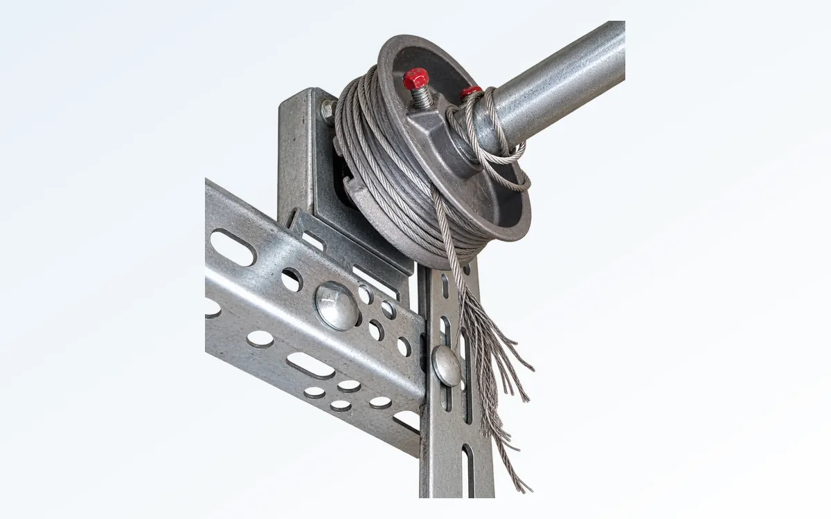 Tambor del cable en el eje de torsión de una puerta de garaje con un cable de elevación deshilachado colgando debajo